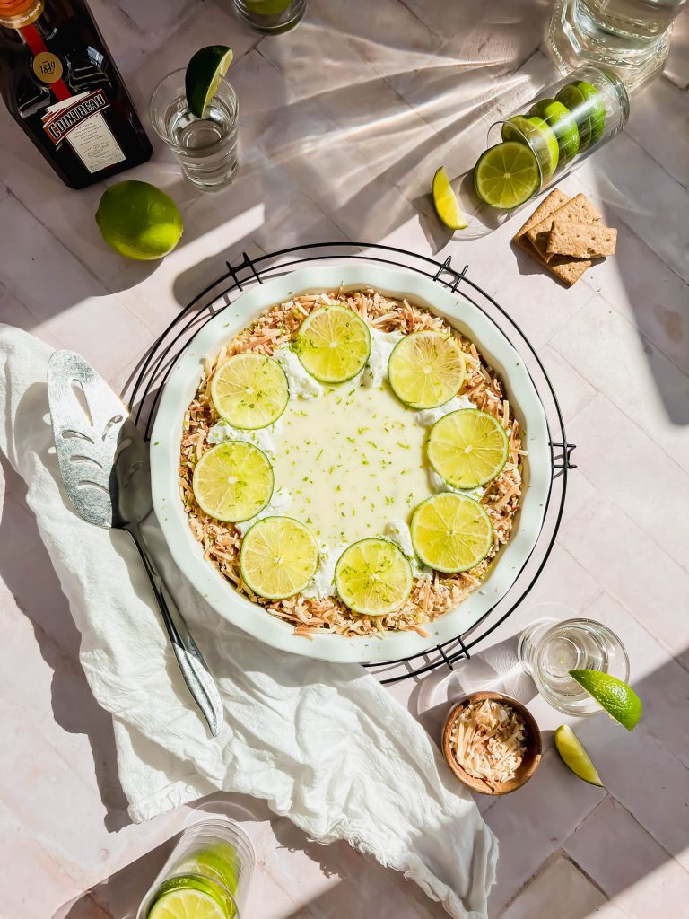 overhead shot of tequila key lime pie in white baking dish surrounded by extra recipe ingredients.