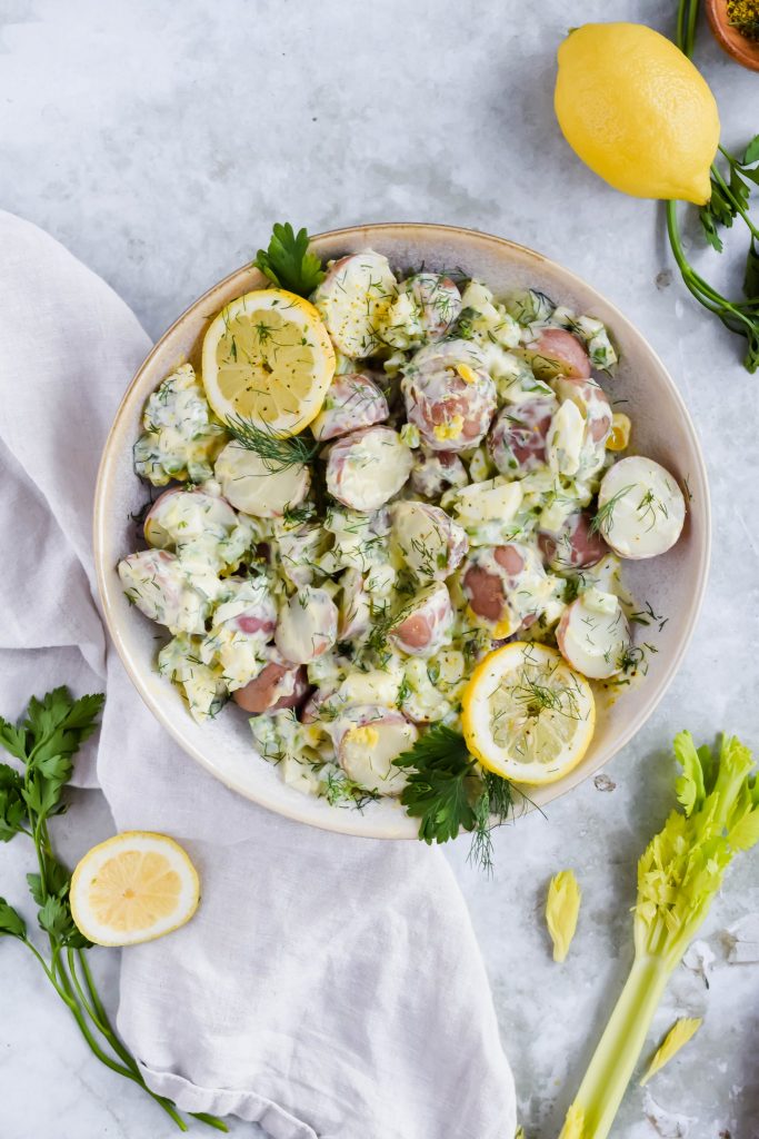 healthy lemon dill potato salad mixed together in white bowl on white background.