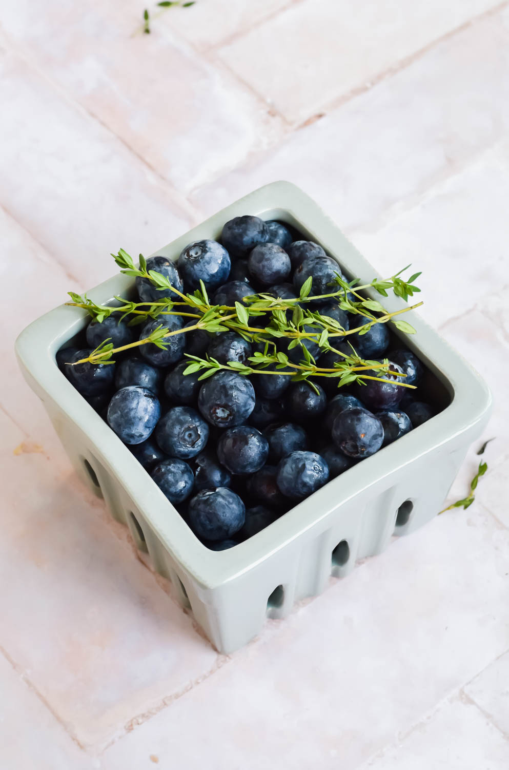 white ceramic basket filled with fresh blueberries with fresh thyme sprigs on top.