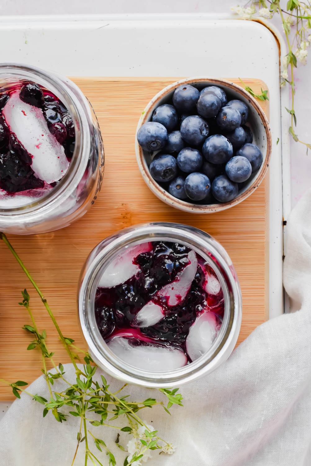 two blueberry vodka lemonades on wood board beside bowl of fresh blueberries.