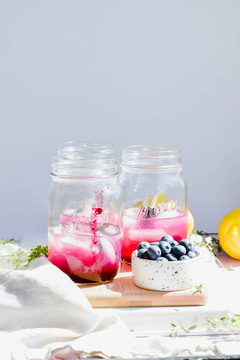three blueberry vodka lemonades on wood board beside bowl of fresh blueberries