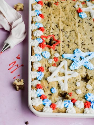 fourth of july cookie cake decorated with red, white and, blue frosting in white baking tray on pink background.