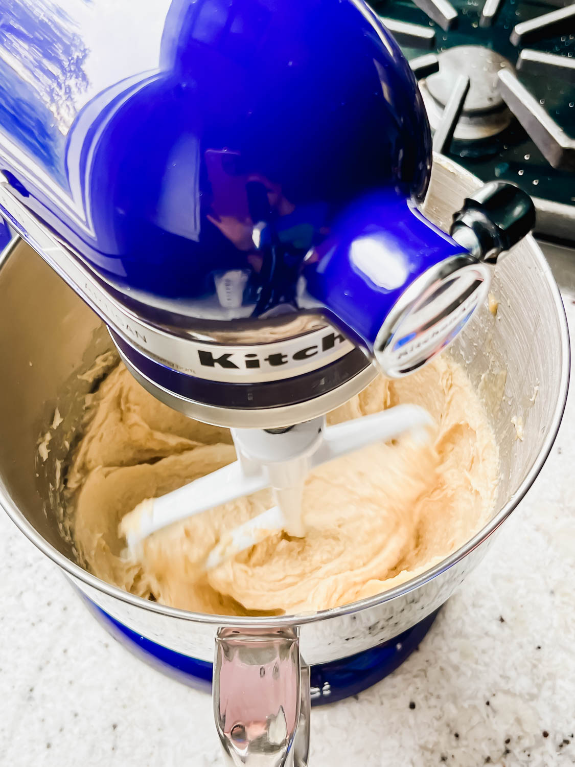 raw cookie dough being mixed in blue stand mixer with stove top in background.