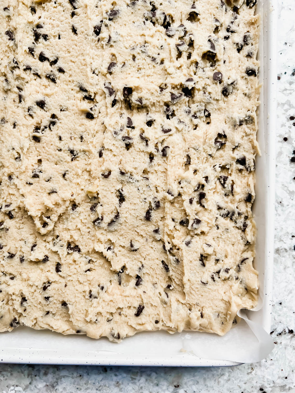 raw cookie cake batter spread in white sheet pan