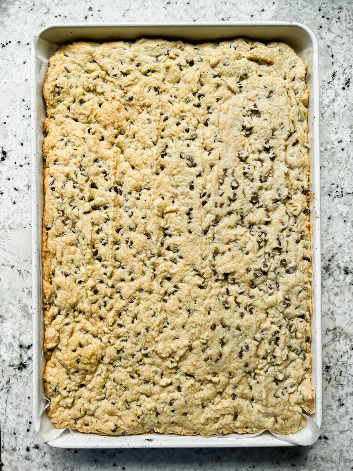 baked chocolate chip cookie cake in rectangular baking sheet on granite counter top.