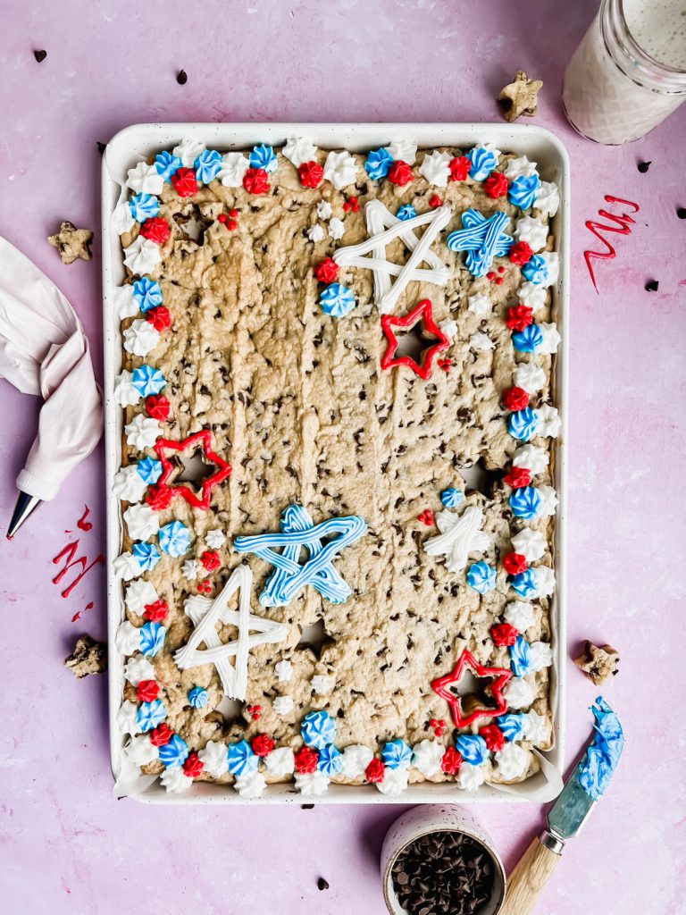 fourth of july cookie cake decorated with red, white and, blue frosting in white baking tray on pink background.
