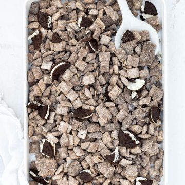finished oreo puppy chow on white baking tray with white spoon in tray on white background.