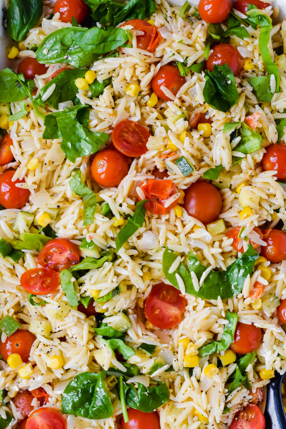 prepared roasted close up shot of summer orzo salad garnished with fresh spinach.