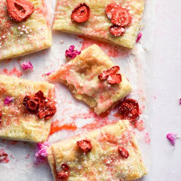 Baked frosted strawberry pop tarts topped with edible flowers and dried strawberries on parchment.