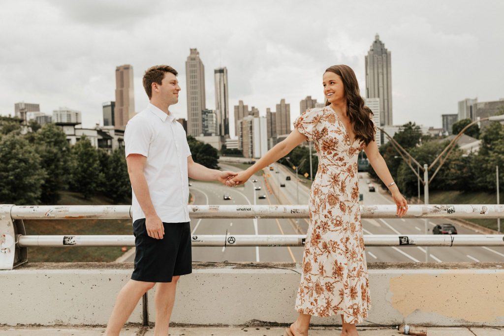 couple walking holding hands on a bridge with cityscape in the background