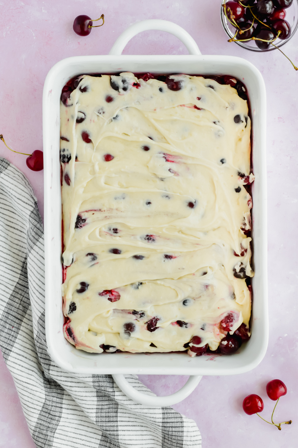 mixed berries and cherries in white baking dish topped with biscuit batter before baking.
