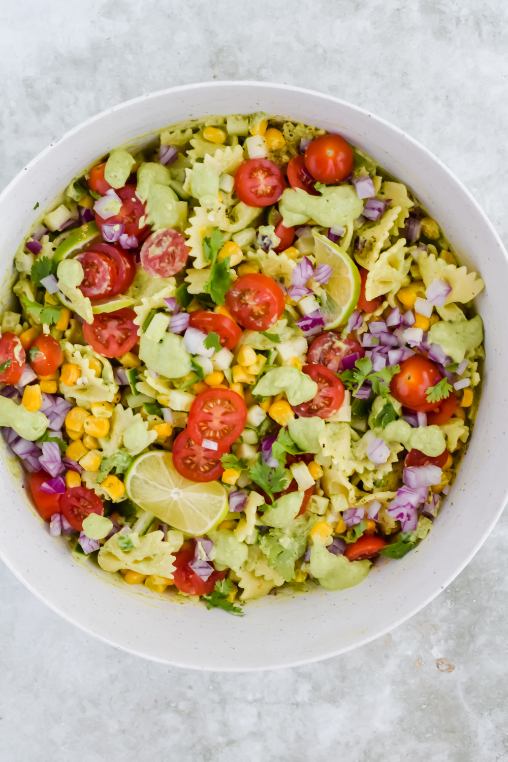 cilantro lime pasta salad tossed in large white mixing bowl on light gray background.