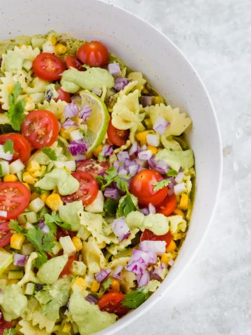 cilantro lime pasta salad tossed in large white mixing bowl on light gray background.