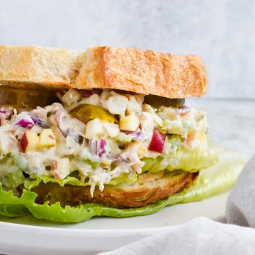 healthy pesto chicken salad between two slices of toasted bread on white plate.