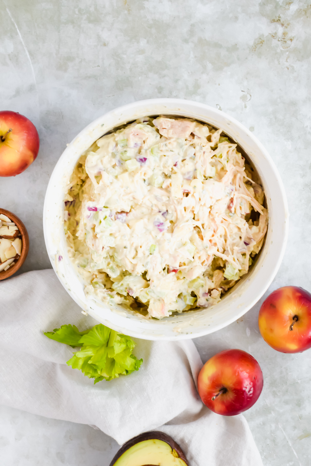 healthy pesto chicken salad mixed in large white bowl with apples and celery leaves surrounding.