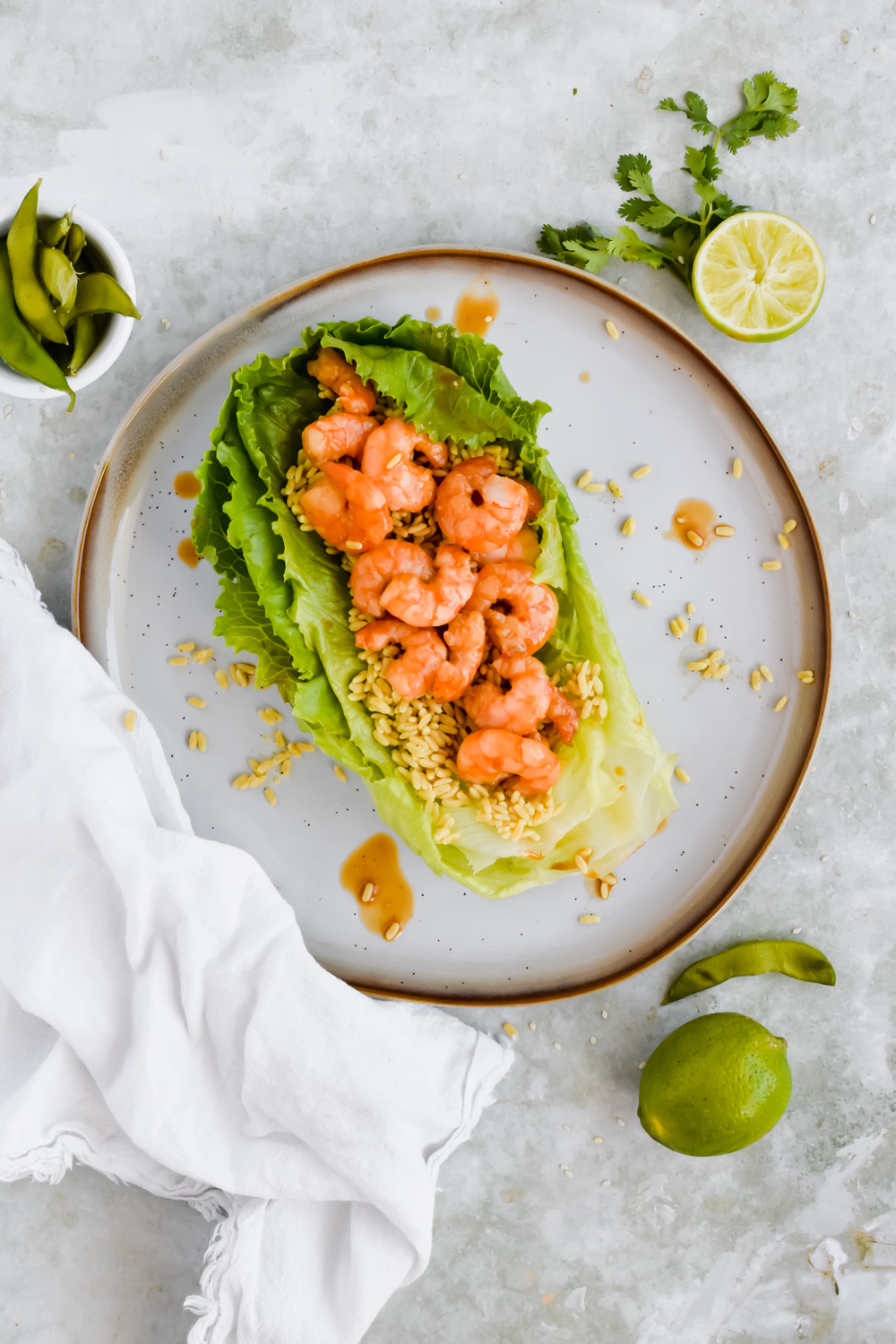 two large slices of romaine lettuce filled with rice and honey teriyaki shrimp on white plate on gray background.