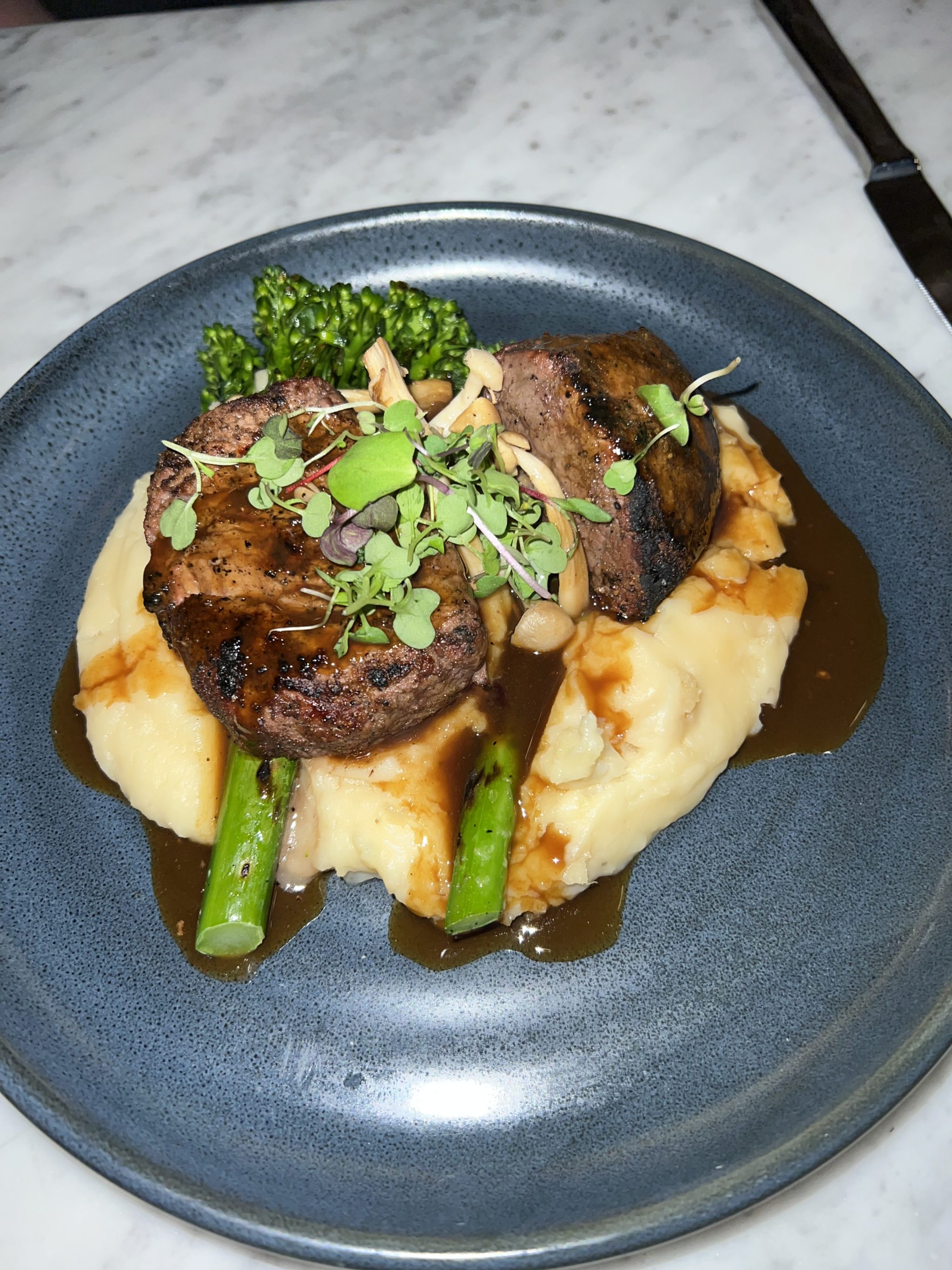 blue plate filled with buttery mashed potatoes topped with asparagus and grilled filet
