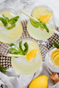 three limoncello spritzes garnished with lemon wedges, mint leaves, and straws in wine glasses.