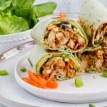 four halves of oriental chicken wraps stacked on one another on white plate with extra lettuce in background.