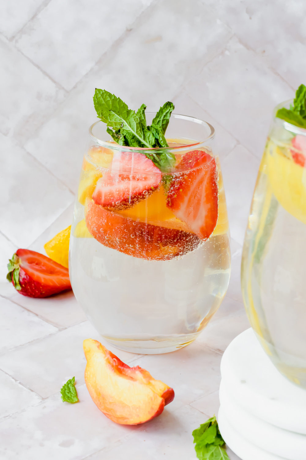 wine glass filled with sparkling white wine peach sangria garnished with fresh mint and berries.