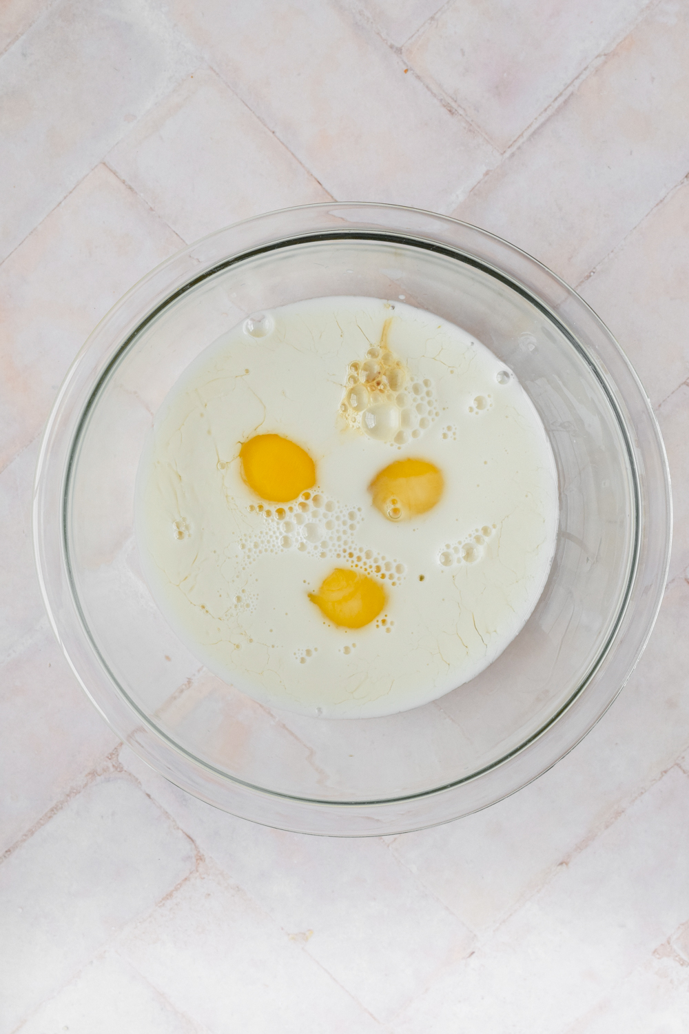 milk and eggs in glass bowl on white stone background.