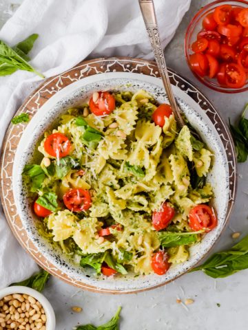 bow tie pasta covered in goat cheese pesto garnished with parmesan and cherry tomatoes in large white bowl.
