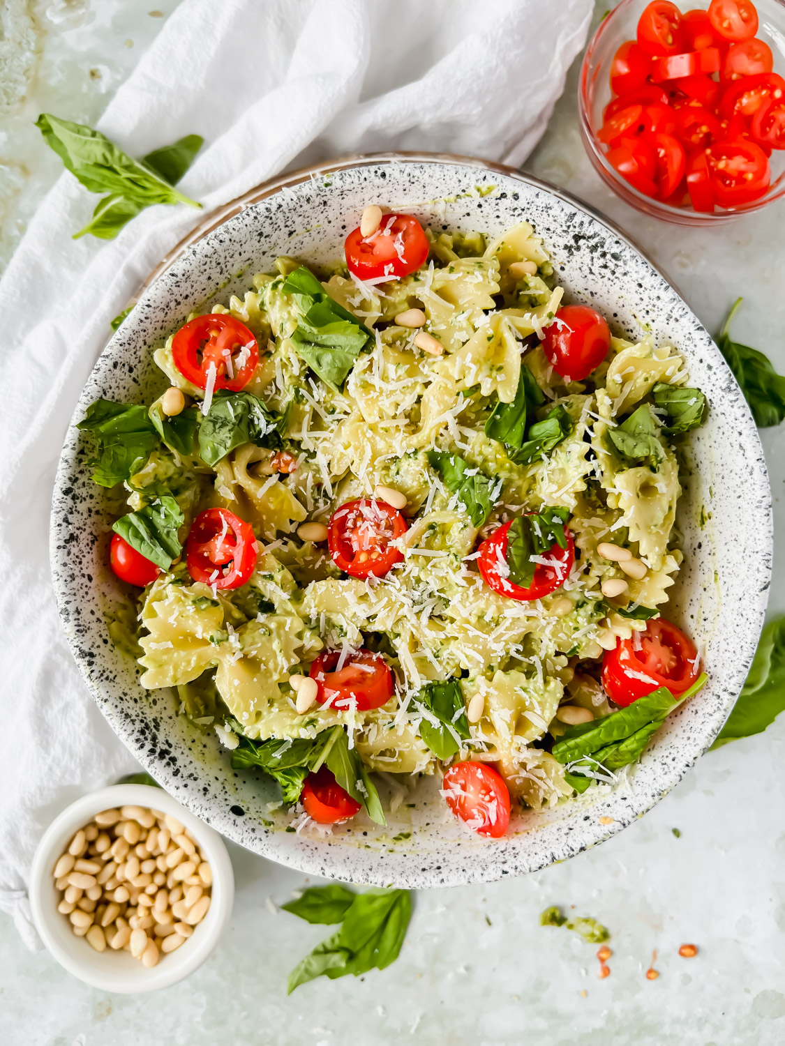 bow tie pasta covered in goat cheese pesto garnished with parmesan and cherry tomatoes in large white bowl.