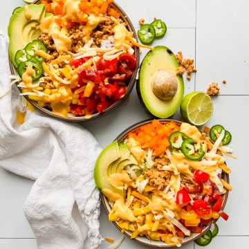 two bowls loaded with taco salad on a white tiled background.