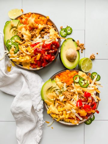 two bowls loaded with taco salad on a white tiled background.