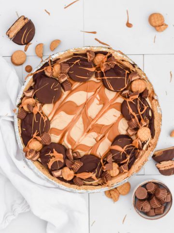 nutter butter pie garnished with chocolate cookies and candy pieces swirled with peanut butter on white background with additional cookies and candies surrounding.