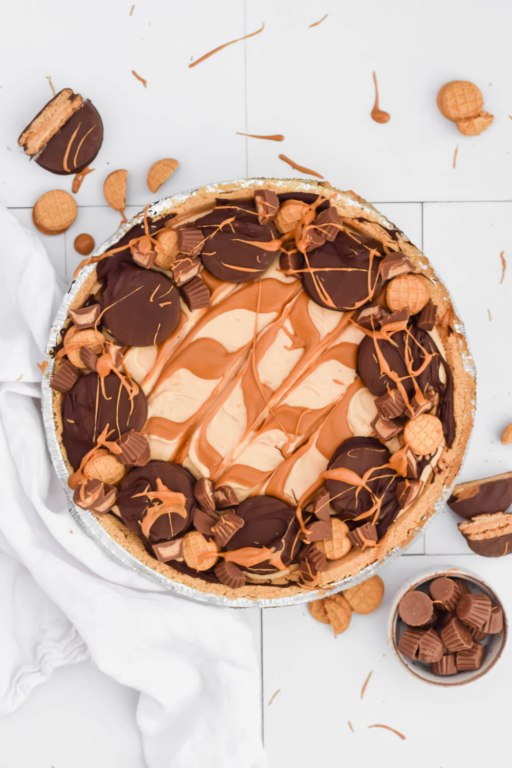 nutter butter pie garnished with chocolate cookies and candy pieces swirled with peanut butter on white background with additional cookies and candies surrounding.