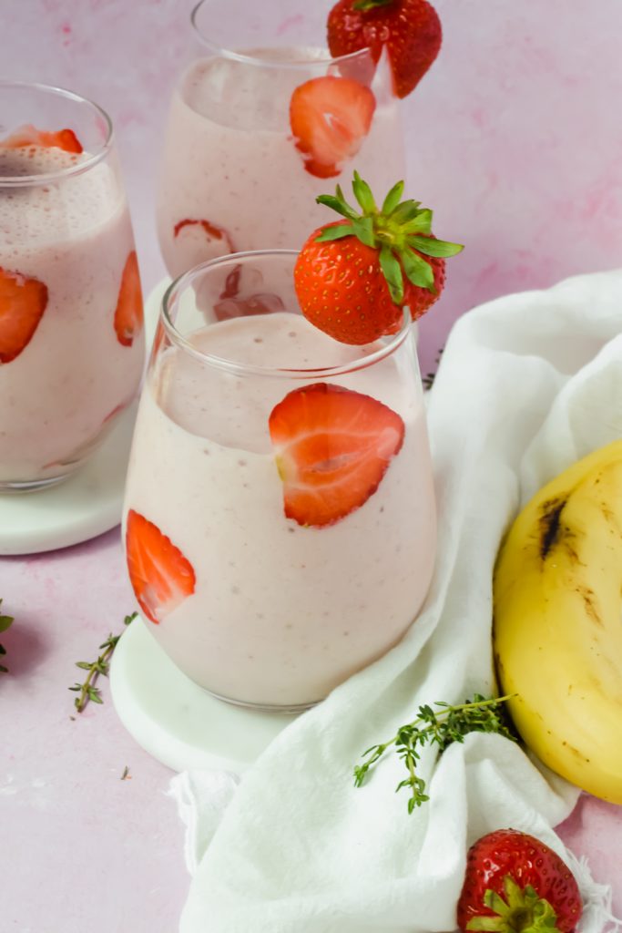 three glasses filled with strawberry banana protein smoothie with strawberry slices lining the glasses.