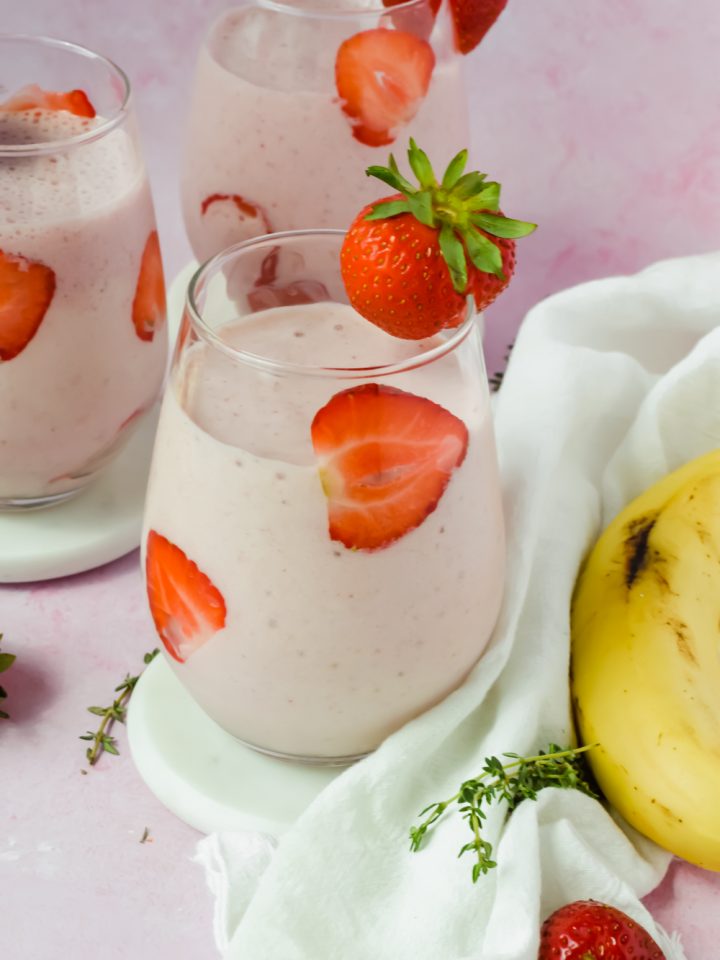 three glasses filled with strawberry banana protein smoothie with strawberry slices lining the glasses.