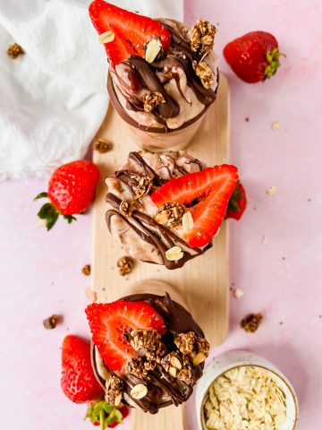 three glasses filled with brownie batter overnight oats and topped with fresh strawberries