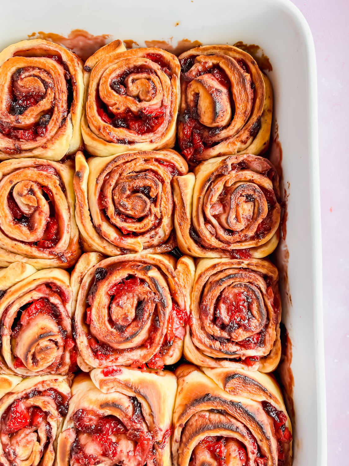 strawberry cinnamon rolls side by side baked in white baking dish.