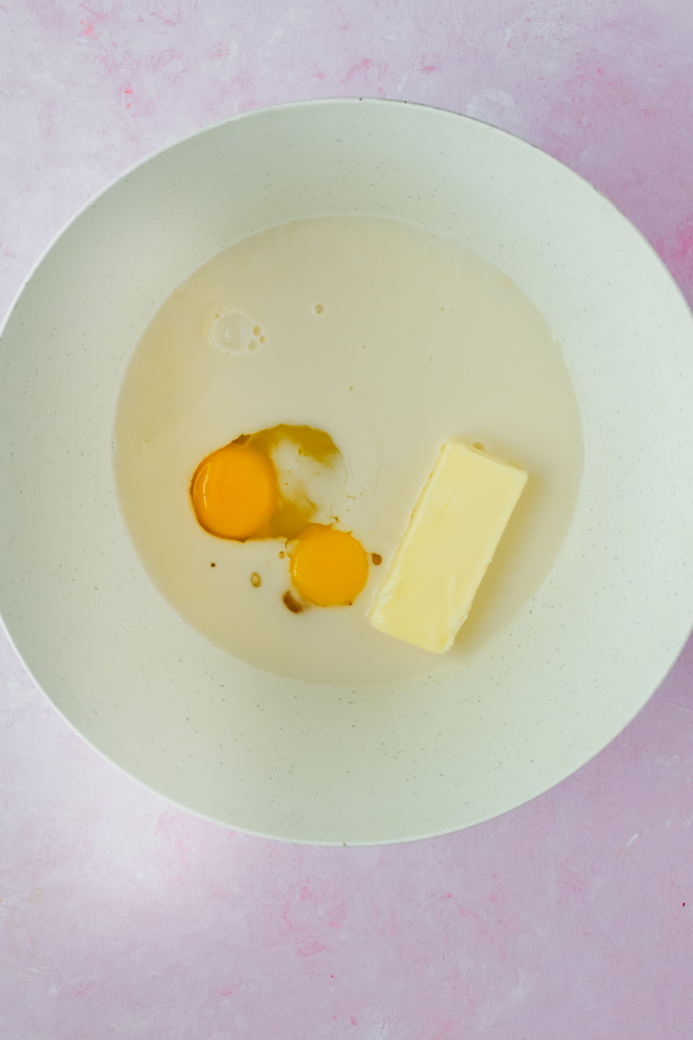 butter, milk and sugar in white bowl on light pink background.