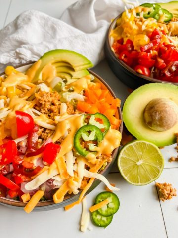 loaded taco salad bowl garnished with jalapenos, avocado, and cheese.