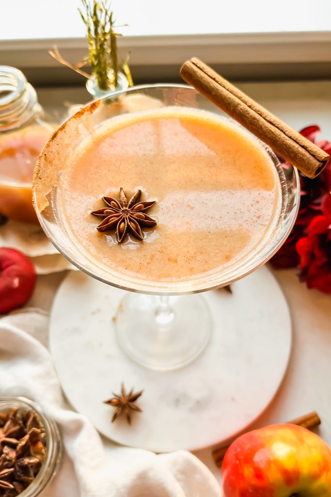 apple pie martini garnished with star anise and cinnamon stick with flowers in background..