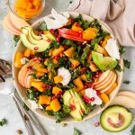 fall kale salad topped with butternut squash cubes, avocado slices, apple slices, pomegranate seeds, and goat cheese.