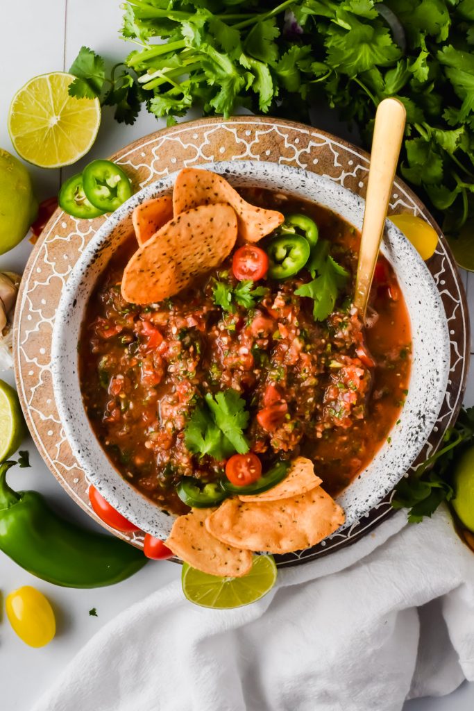 food processor salsa in white serving bowl garnished with cilantro and tortilla chips surrounded by additional recipe ingredients.