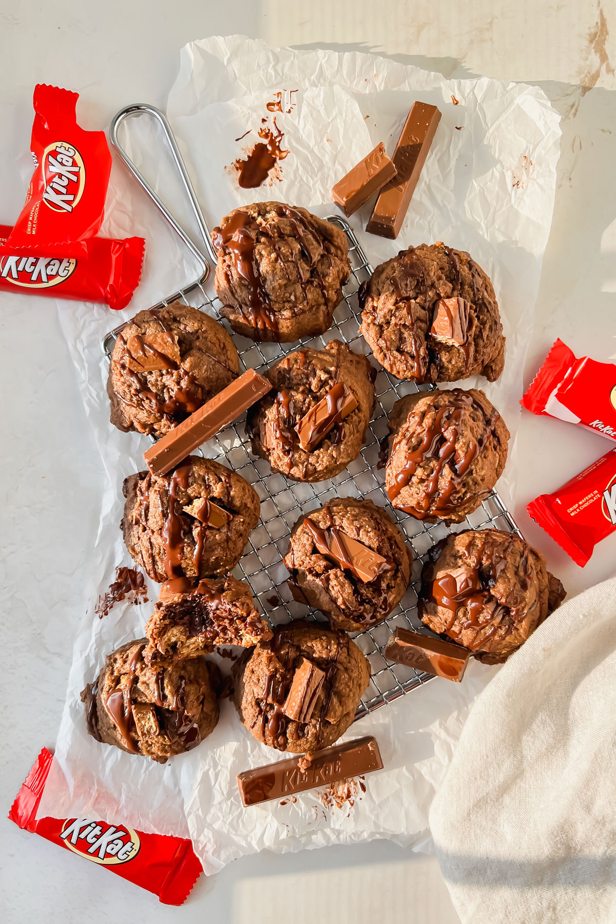 baked kit kat cookies on cooling rack on top of parchment paper with additional kit kats and kit kat wrappers scattered around.