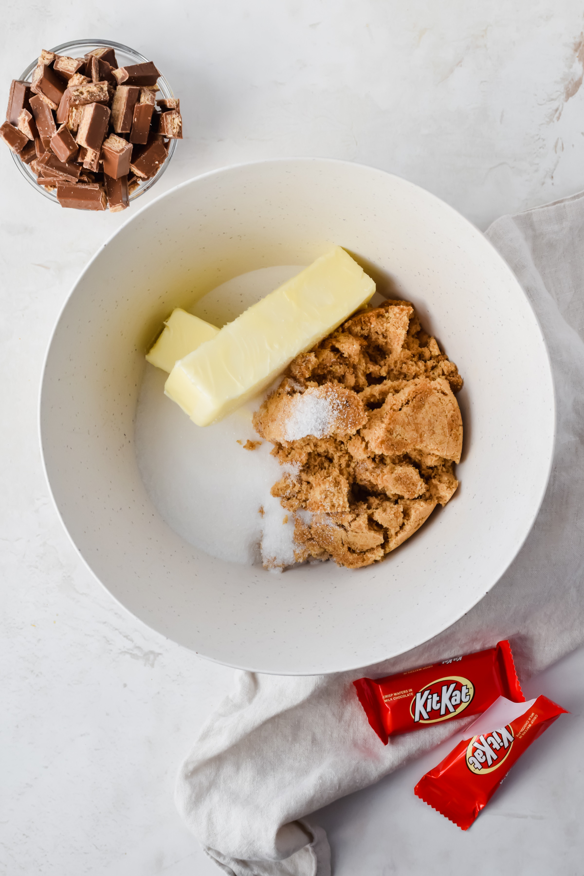 butter and sugar in white mixing bowl before mixing with small bowl of chopped kit kats beside bowl.
