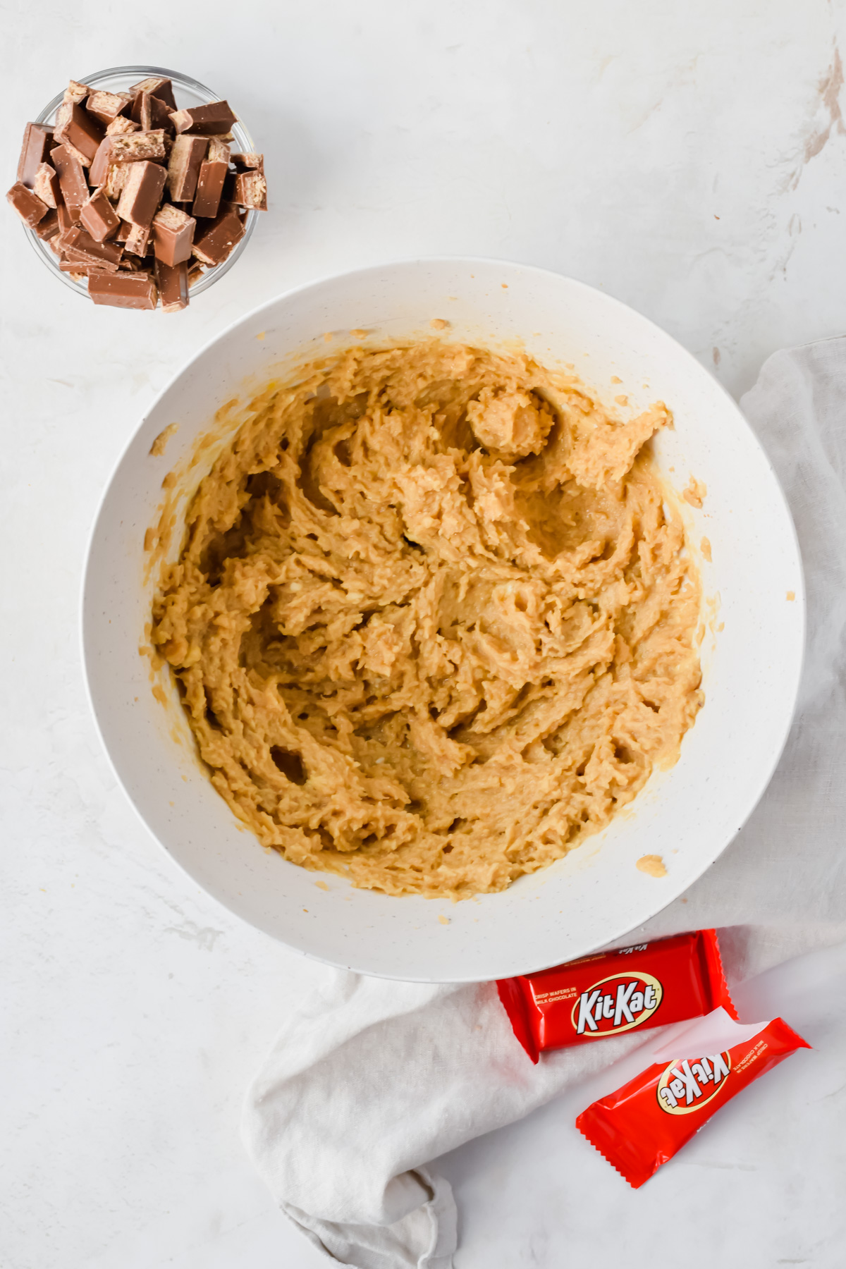 butter and sugar creamed together in white mixing bowl with small bowl of chopped kit kats beside bowl.