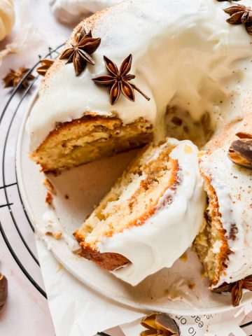 maple bundt cake with cream cheese filling topped with cream cheese frosting and star anise garnish with slice taken out of cake.