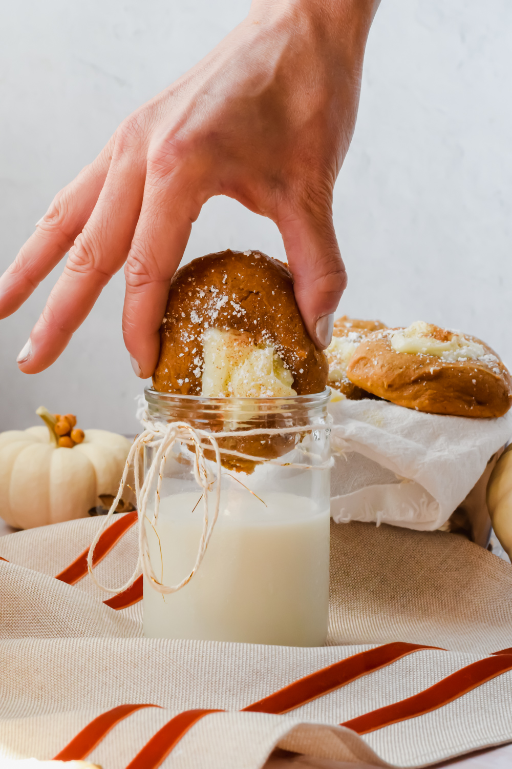 hand dunking pumpkin cheesecake cookie into glass of milk with additional cookies in background.
