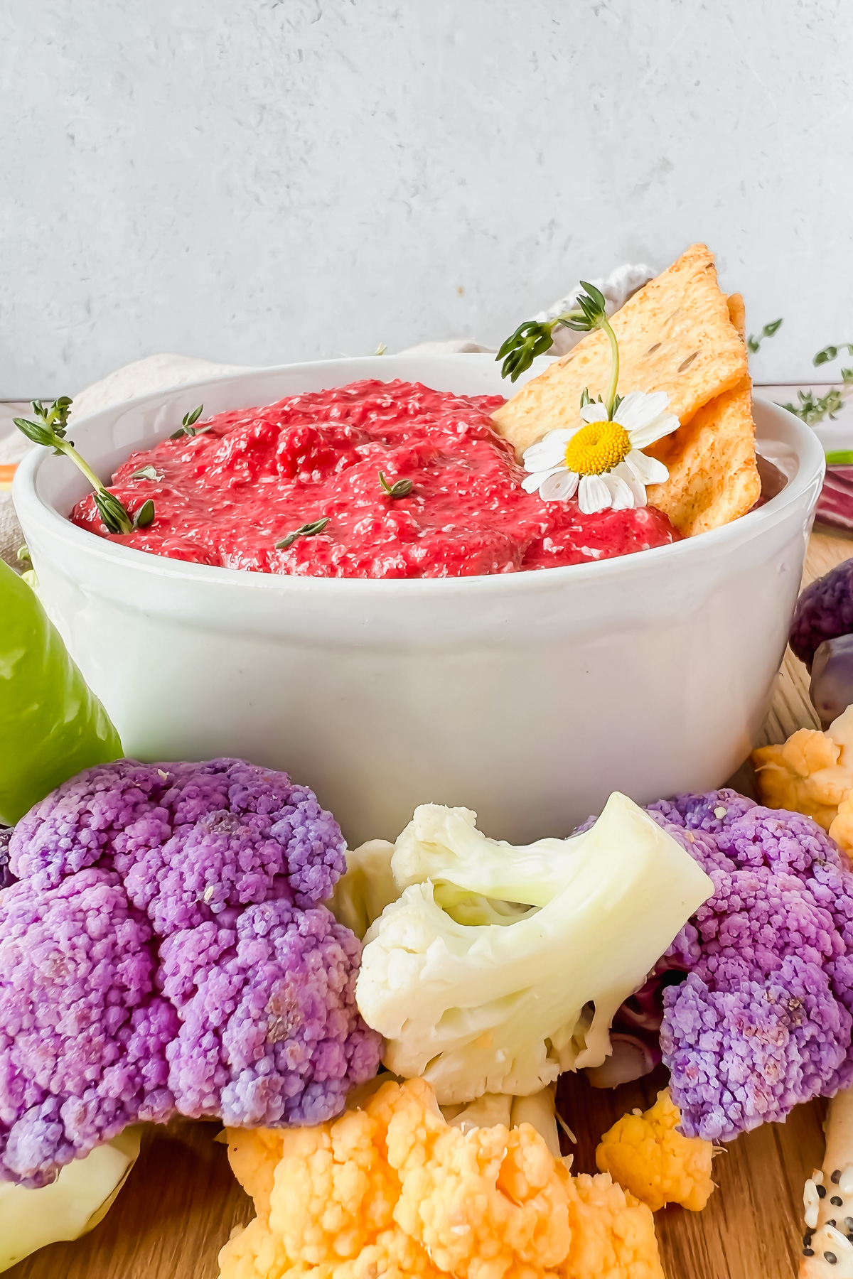 roasted beet dip in white bowl surrounded by multi colored cauliflower.
