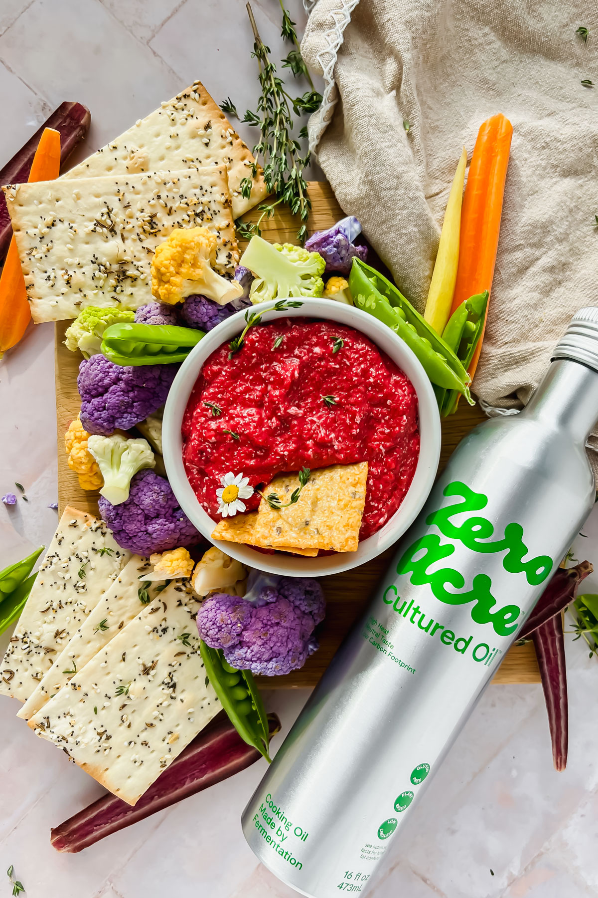 roasted beet dip in white bowl surrounded by cauliflower, crackers, carrots, fresh herbs and a bottle of zero acre cultured oil.