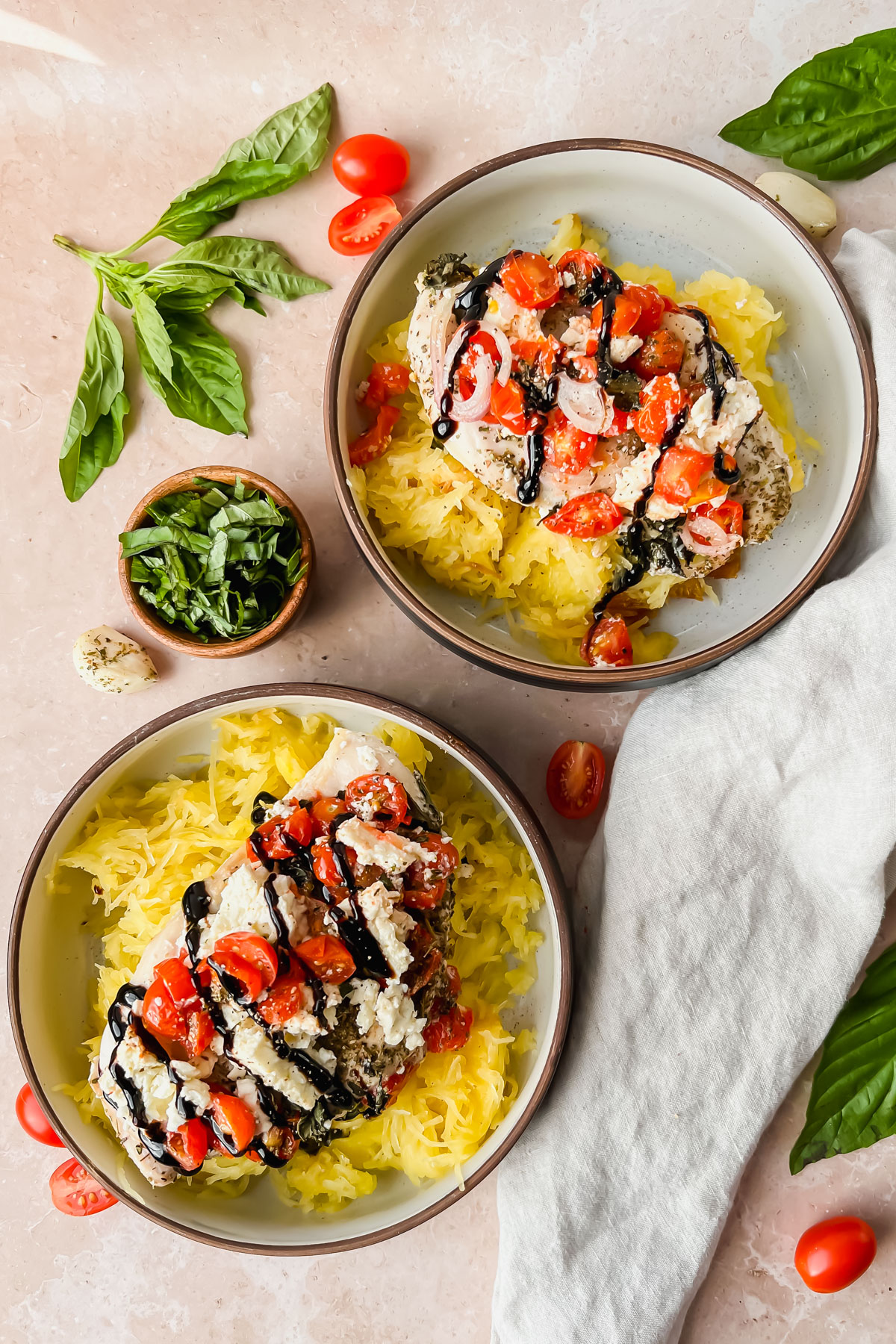 two serving bowls of spaghetti squash topped with baked feta chicken and drizzled with balsamic glaze.