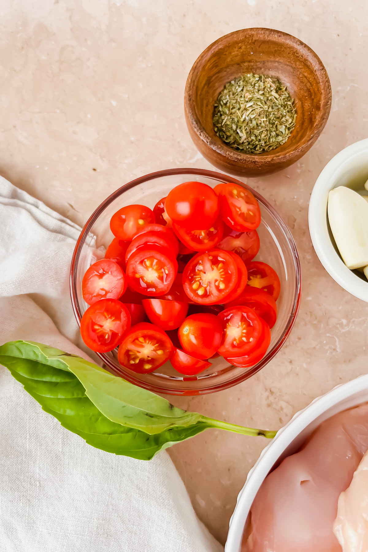 sliced cherry tomatoes in glass bowl beside smaller wood bowl filled with italian spices.