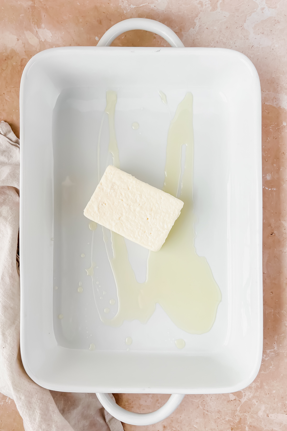 block of feta in white baking dish greased with olive oil.